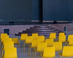 Sillas amarillas en un auditorio con fondo oscuro y luz tenue.