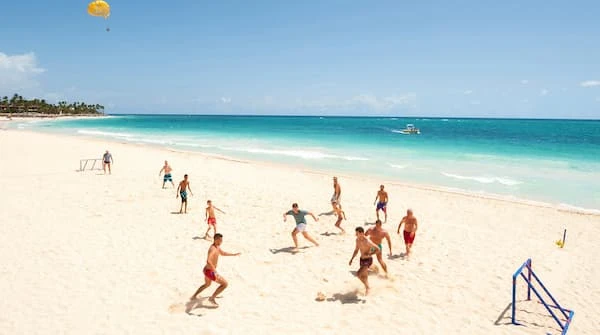 Personas jugando en la playa con mar turquesa y cielo despejado.
