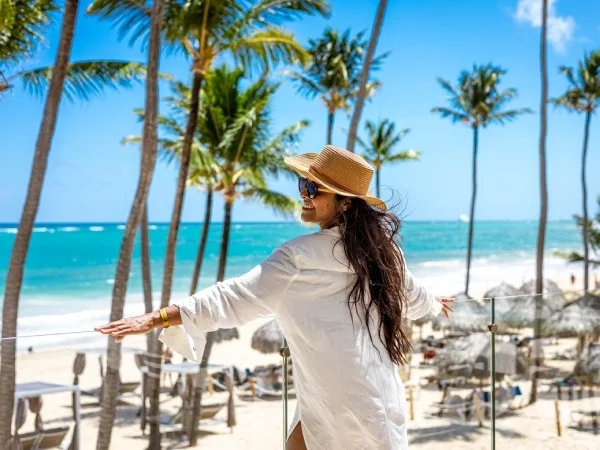 Mujer con sombrero en la playa tropical, palmeras y mar azul al fondo
