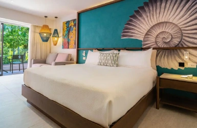 Habitaci&oacute;n hotelera con cama, cabecero decorado y luces colgantes.