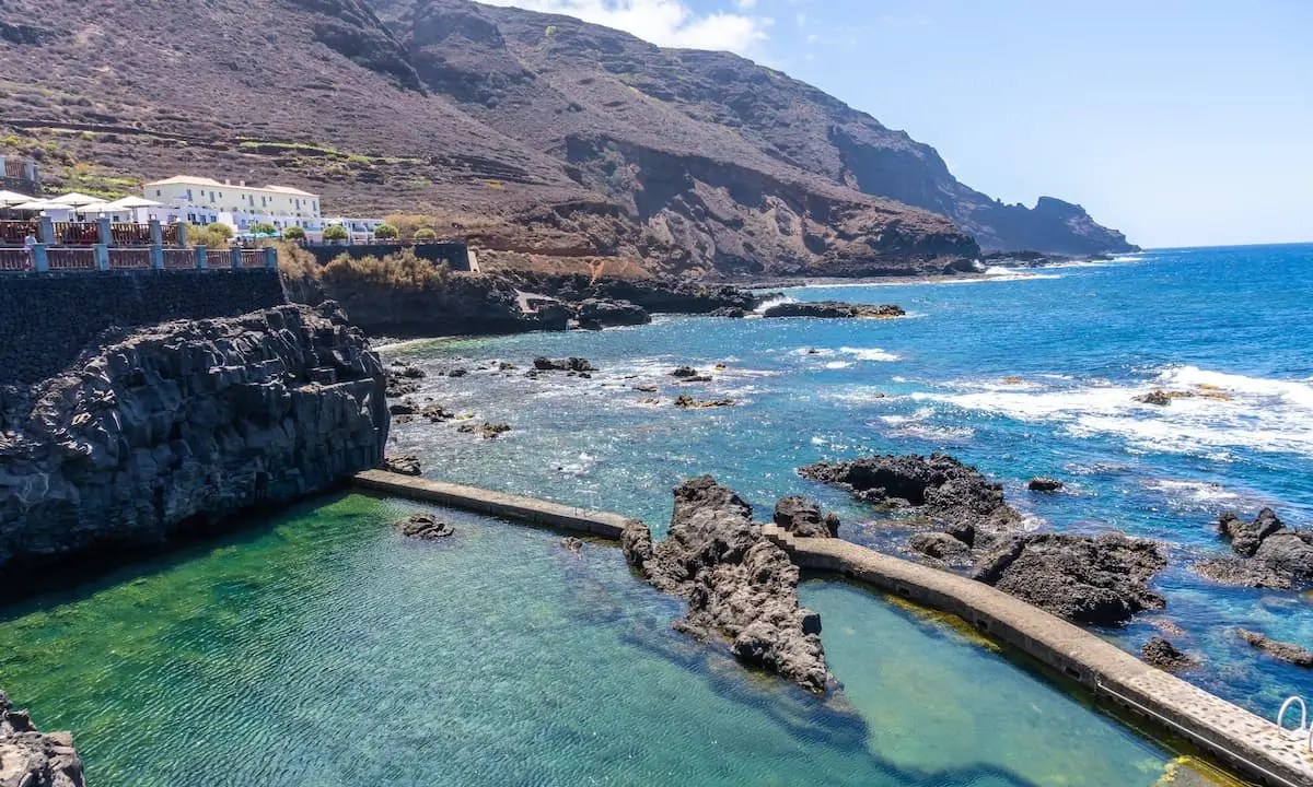 Acantilados y costa oce&aacute;nica con piscinas naturales junto a un hotel blanco
