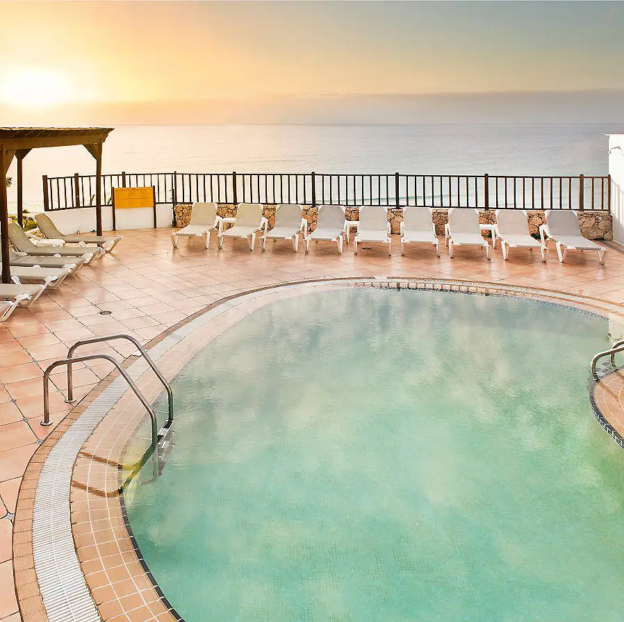 Piscina climatizada con tumbonas y vistas al mar al atardecer.