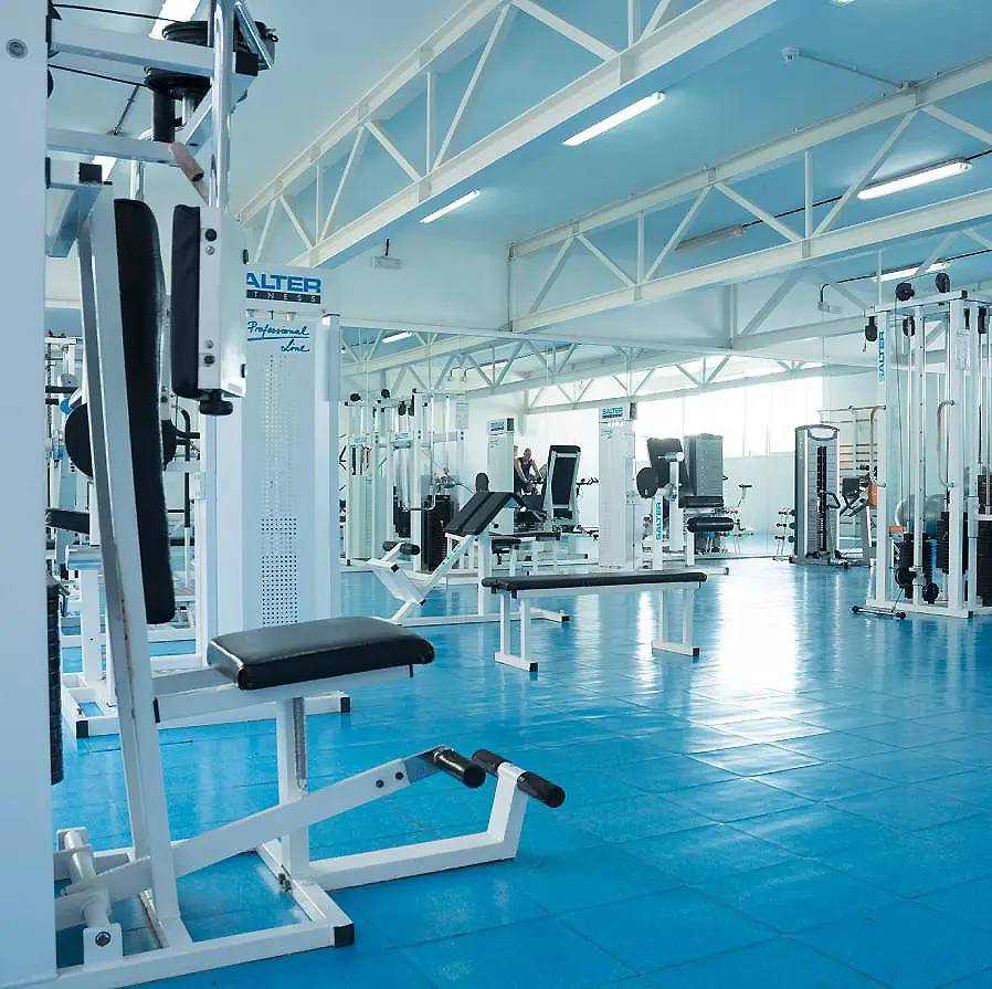 Gimnasio moderno con m&aacute;quinas de entrenamiento y banco en piso azul