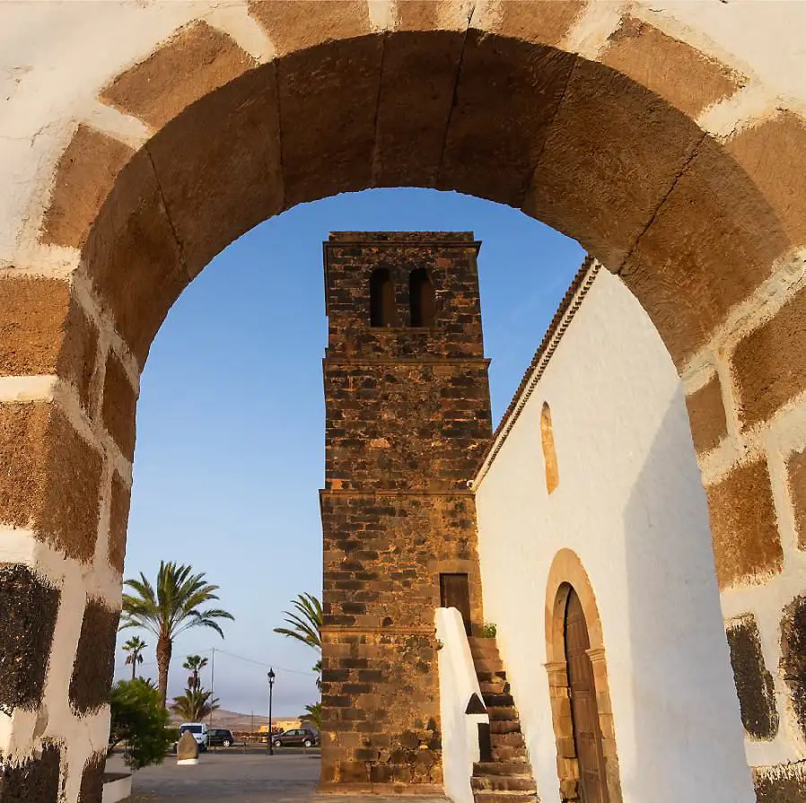 Arco de piedra y torre de ladrillo con palmeras y cielo azul