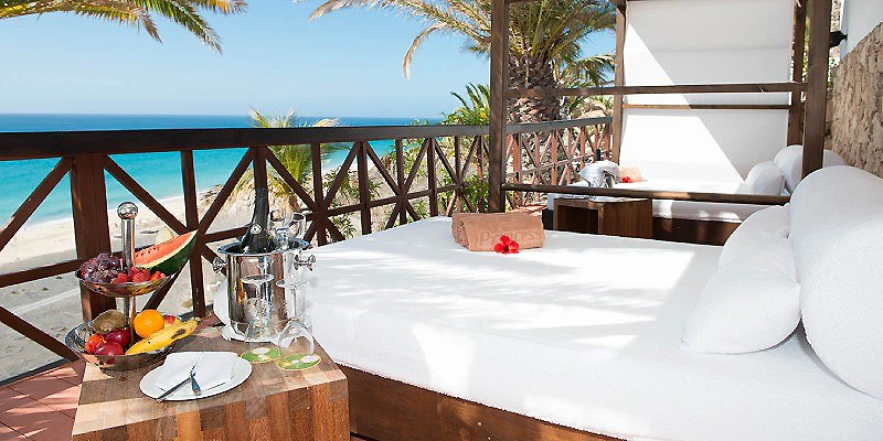 Mesa con desayuno y vista al mar desde una terraza con palmeras