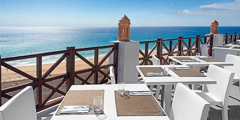 Terraza con mesas blancas frente al mar azul y barandillas de madera