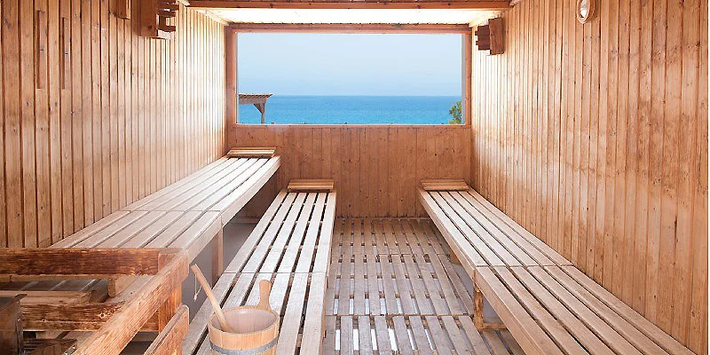 Interior de una sauna de madera con ventana al mar y bancos.