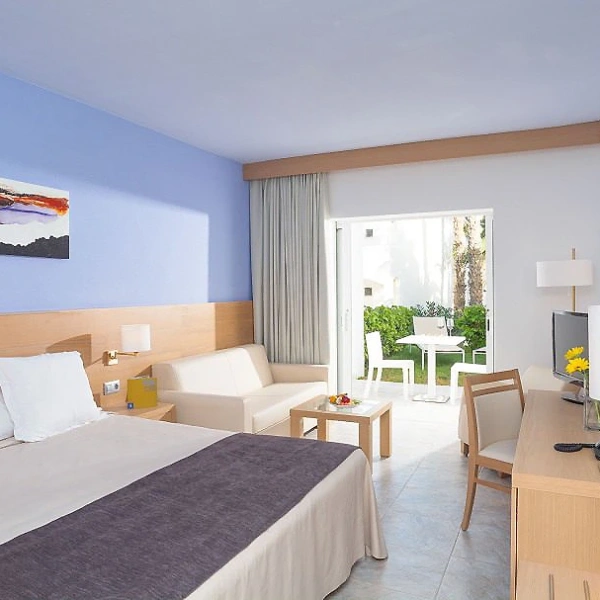 Habitaci&oacute;n de hotel moderna con cama, zona de estar y balc&oacute;n con mesa exterior.