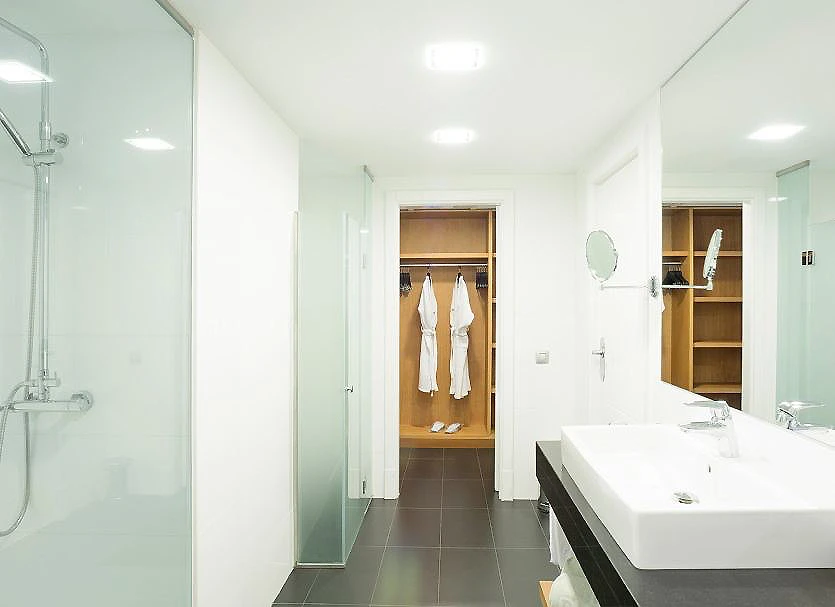 Ba&ntilde;o moderno con ducha de vidrio, lavabo blanco y armario abierto.