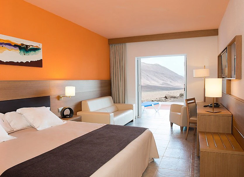 Habitaci&oacute;n de hotel moderna con cama, sillones y vista a monta&ntilde;as nevadas
