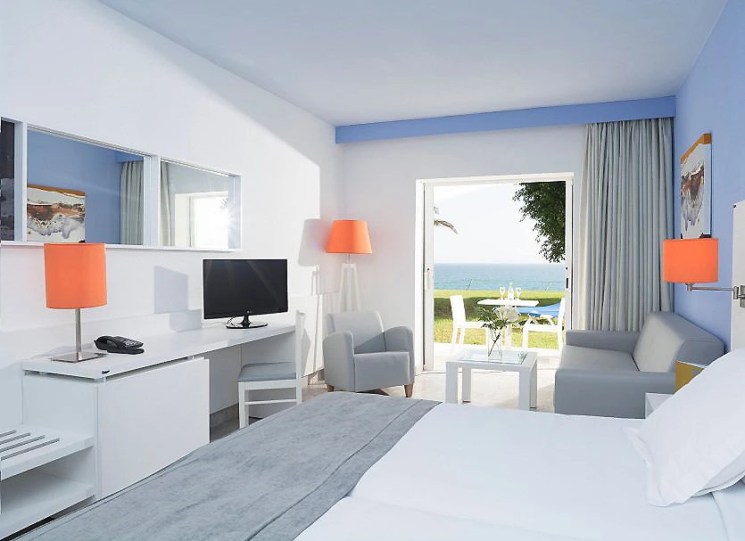 Dormitorio moderno con cama, sillones y vista al mar, l&aacute;mparas naranjas