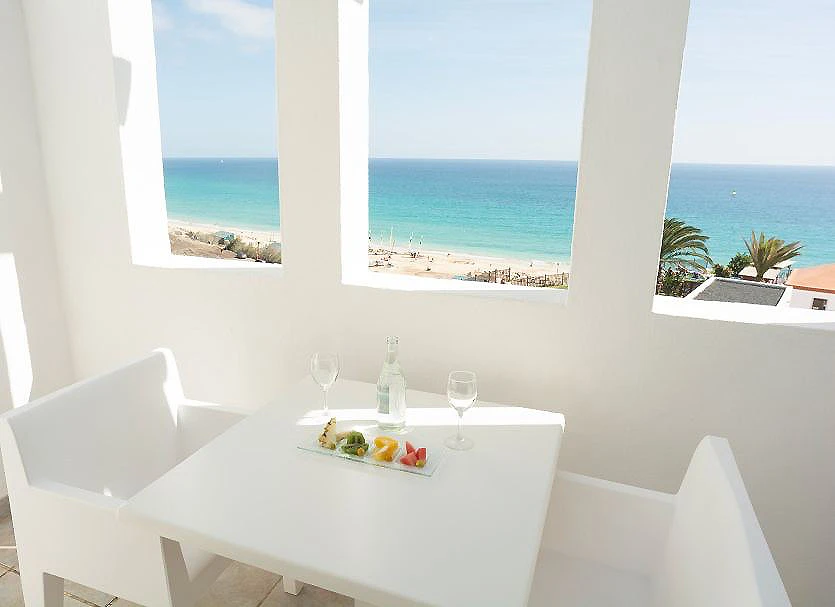 Mesa blanca con frutas y copas, vista al mar desde balc&oacute;n con columnas