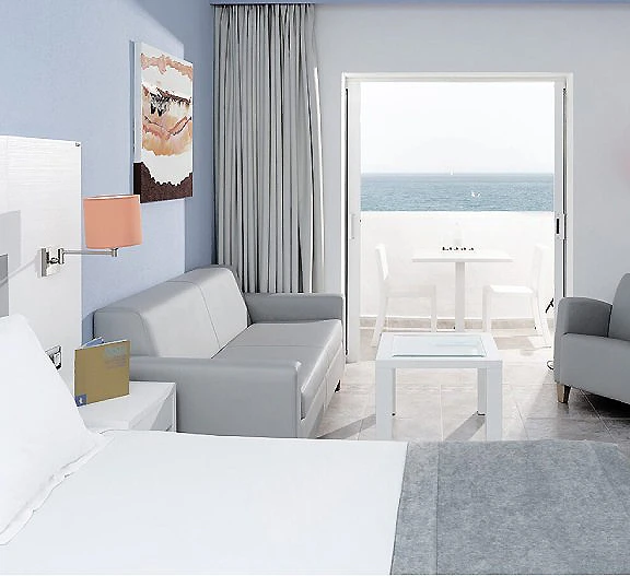 Sala de estar moderna con sof&aacute; y vista al mar por una ventana.