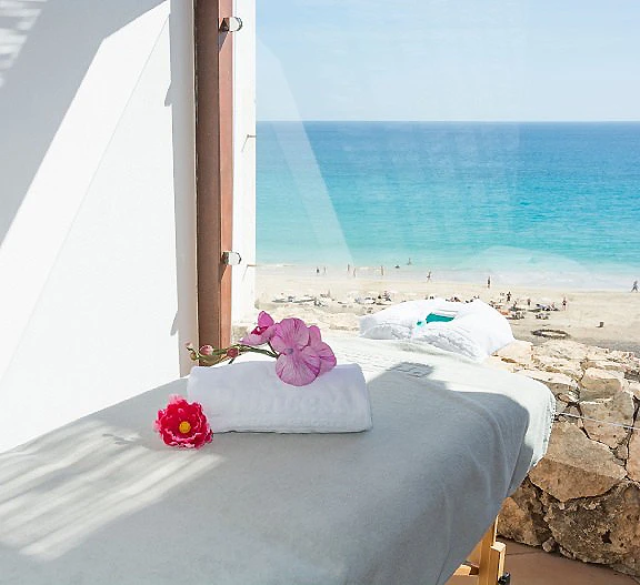 Cama con toallas y flores junto al mar, vista desde una terraza blanca.