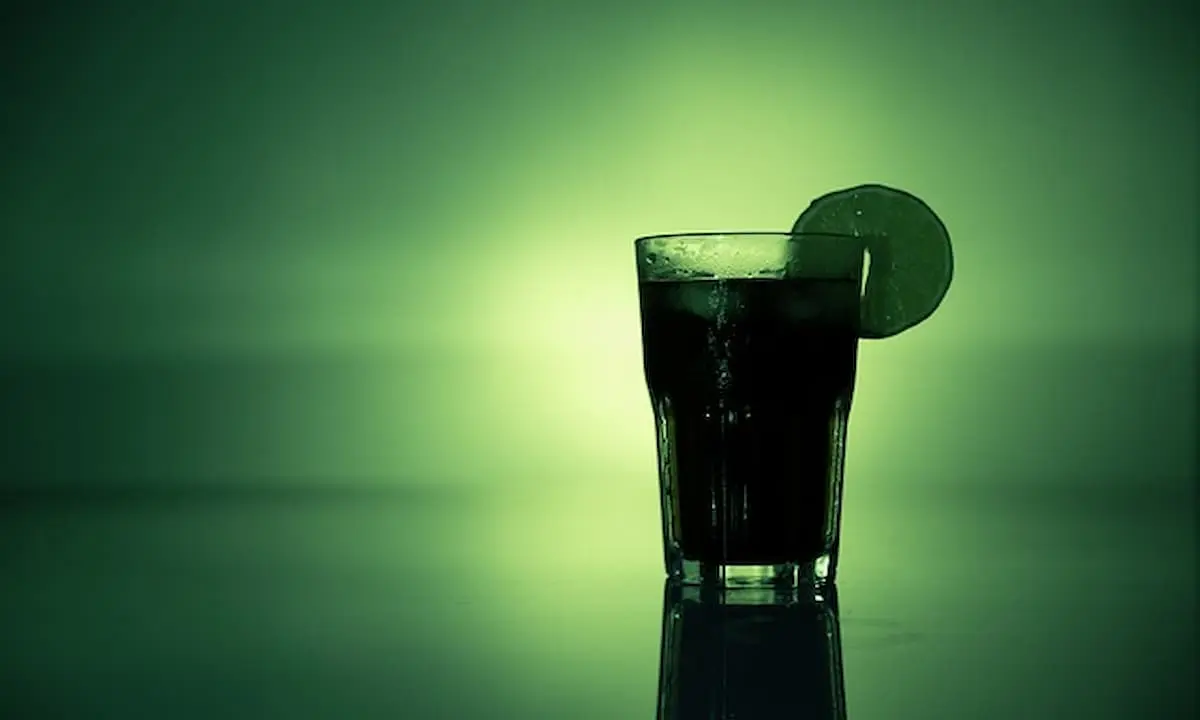 Vaso oscuro con hielo y lim&oacute;n sobre fondo verde desenfocado.
