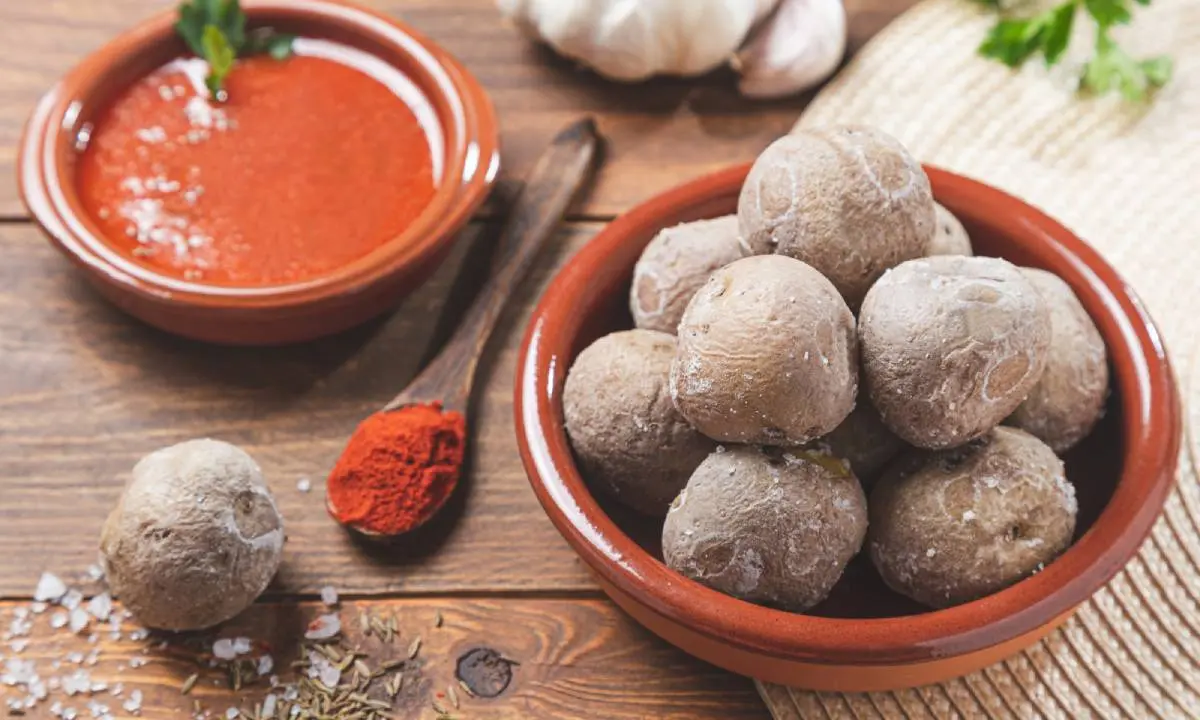 Bol de alb&oacute;ndigas de pan y salsa roja en cuencos de barro sobre mesa de madera