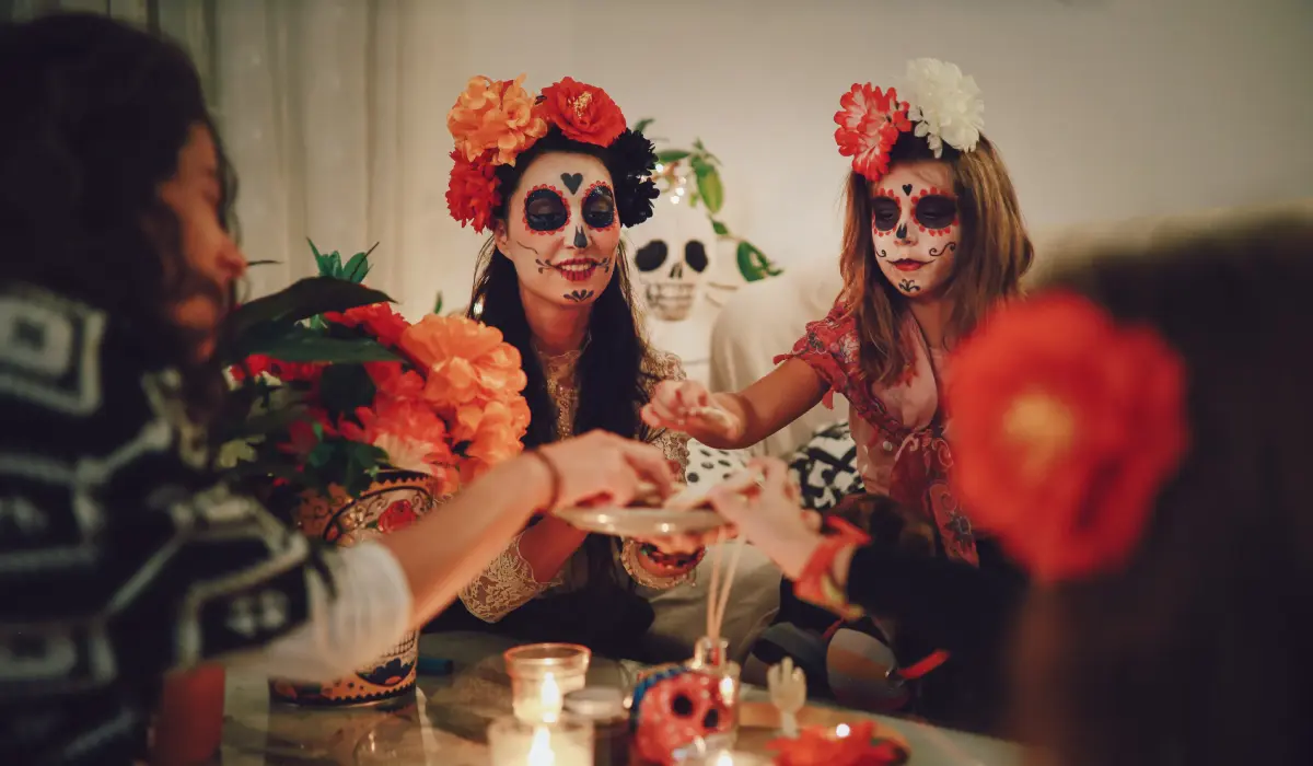 Dos mujeres con maquillaje de calavera y flores celebrando un cumplea&ntilde;os en la mesa