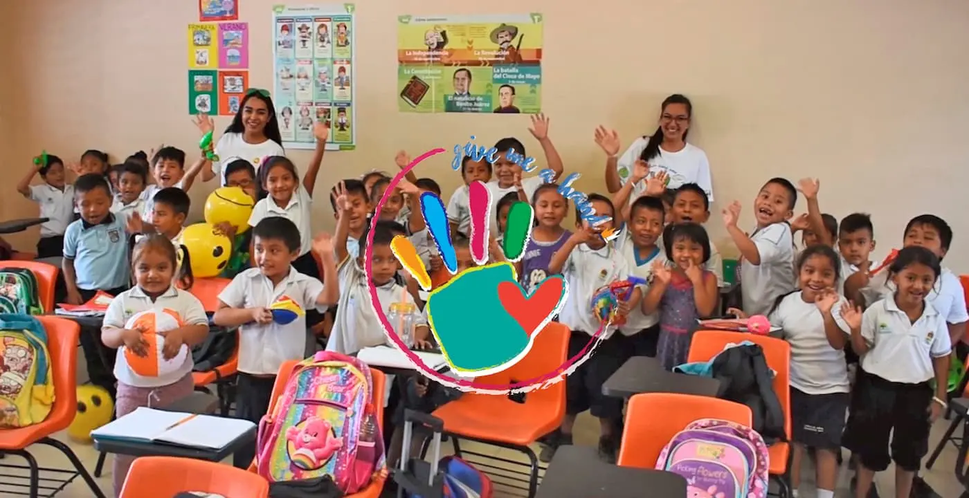 Ni&ntilde;os y maestros sonrientes en el aula, con mochilas y globos coloridos.