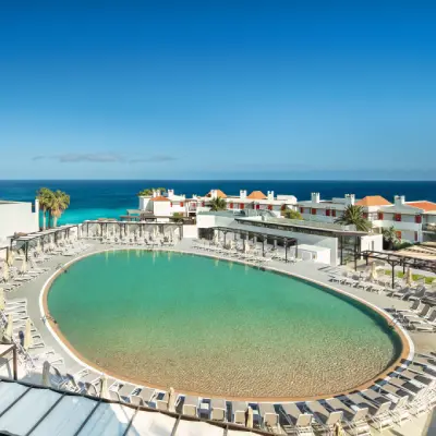 Piscina turquesa con tumbonas frente al mar y edificios blancos