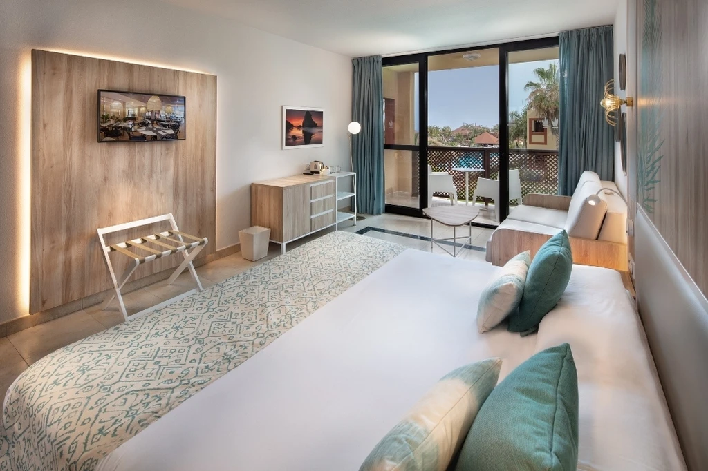 Dormitorio moderno con cama, sillones y cortinas verdes, ventana al balc&oacute;n