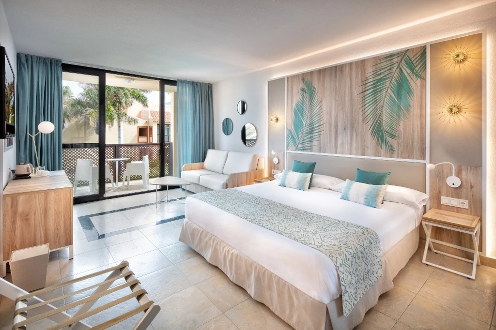 Dormitorio moderno con camas, cortinas azules y pared con hojas tropicales