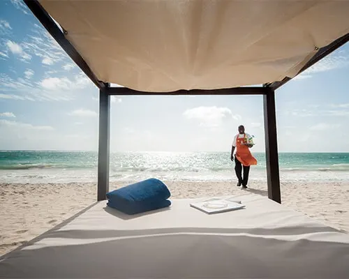 Persona con bolsa naranja en playa, bajo una estructura de lona abierta.