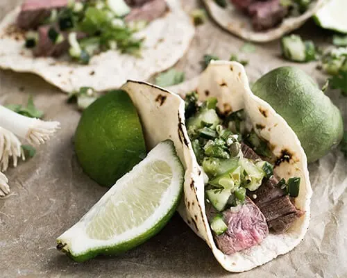 Tacos con nopales y carne, servidos en tortillas con lim&oacute;n y salsa.