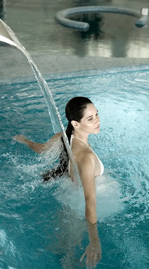 Mujer en una piscina, sujetando la baranda y salpicando agua