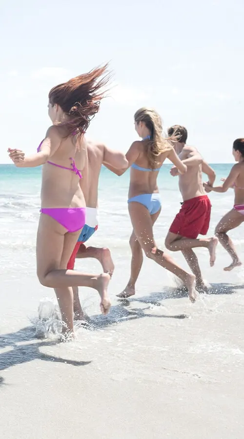 Ni&ntilde;as jugando y corriendo en la playa, salpicando agua, con sol y mar.