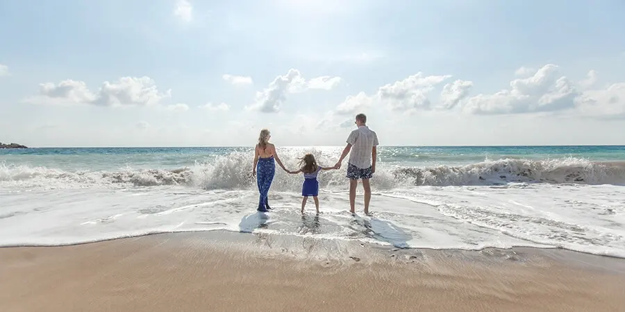 Familia tom&aacute;ndose de la mano en la playa, con el mar y olas al fondo