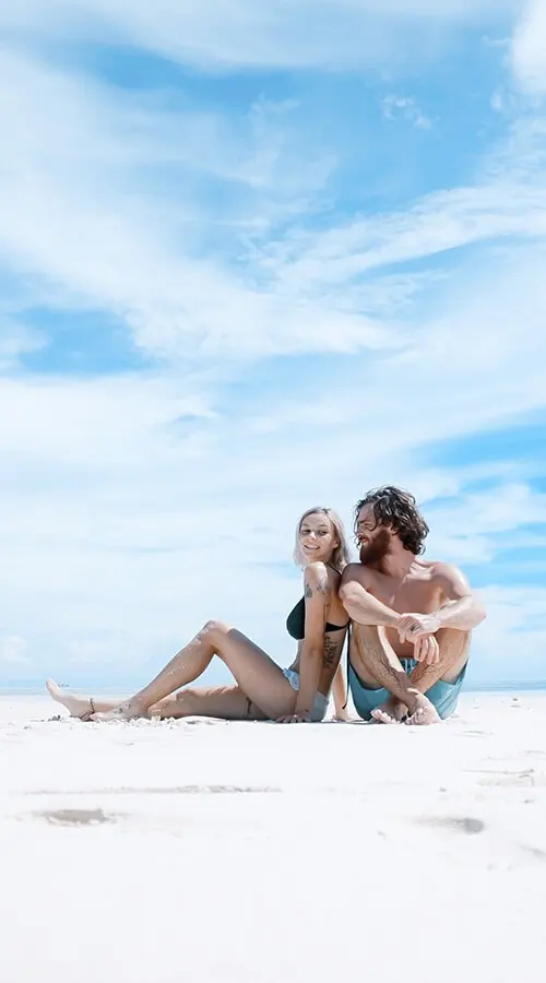 Pareja en la playa de arena blanca, sentados juntos bajo el cielo azul