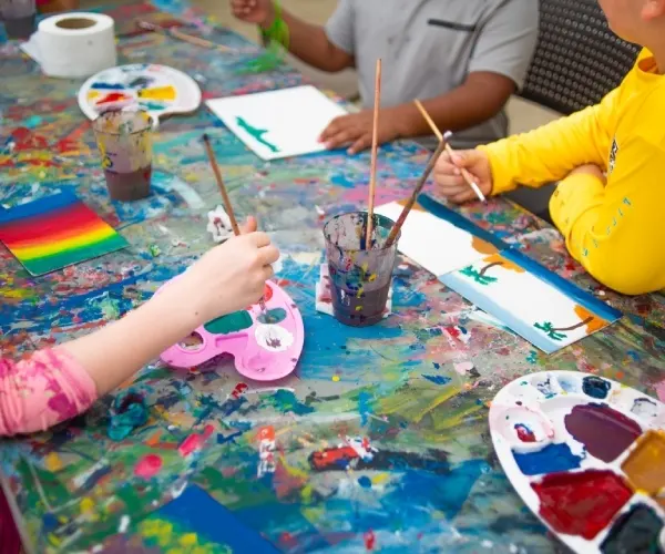 Ni&ntilde;os pintando con pinceles sobre una mesa de colores y papel blanco