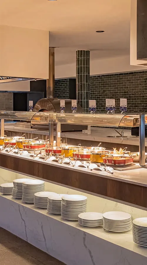 Mesa de buffet con bandejas y platos apilados en un comedor hotelero.