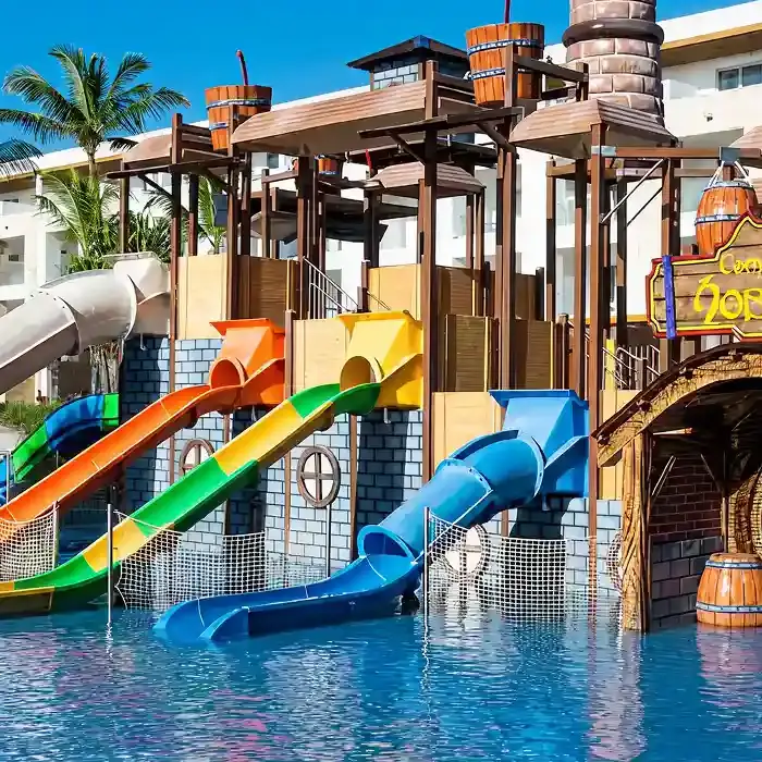 Toboganes de colores en un parque acu&aacute;tico con piscina y palmeras.