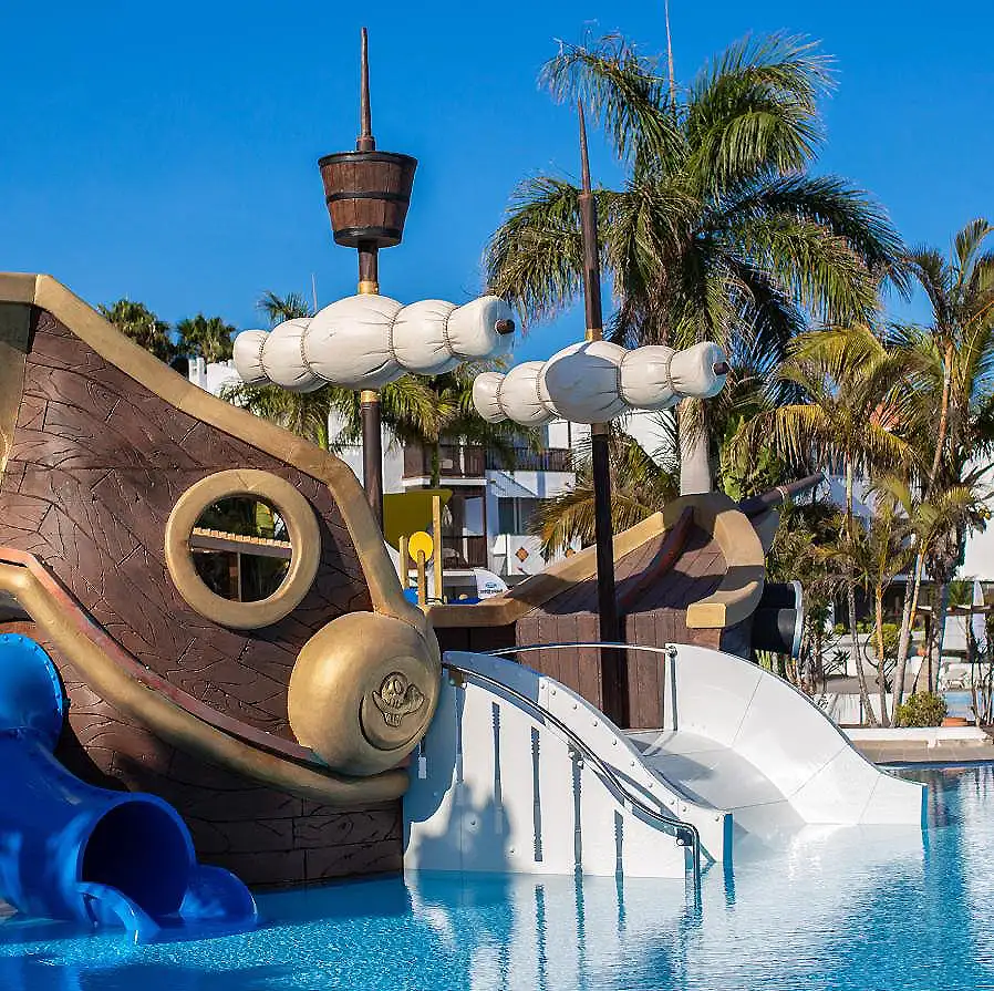 Tobog&aacute;n acu&aacute;tico blanco y dorado con palmeras y piscina azul al fondo.