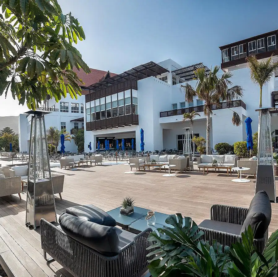 Terraza moderna con piscina de madera, palmeras y edificio blanco al sol