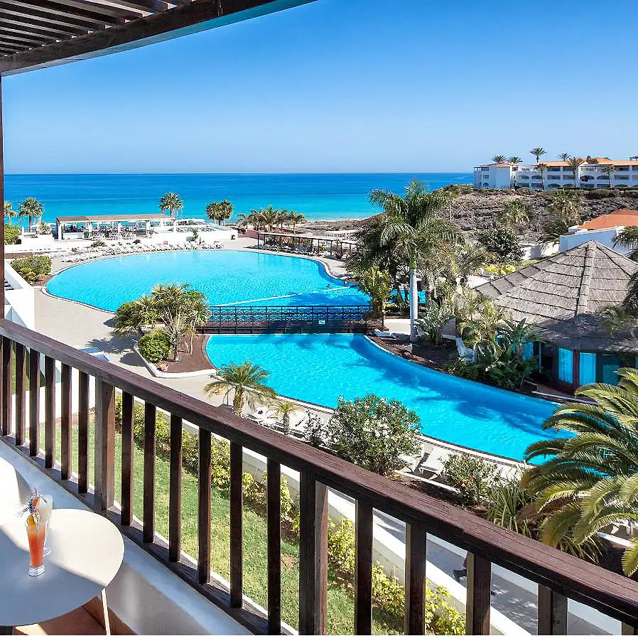 Piscina azul junto al mar con palmeras y terraza frente a la costa