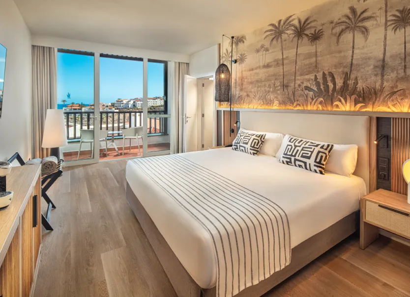 Habitaci&oacute;n de hotel moderna con cama, cojines y balc&oacute;n con vista al mar