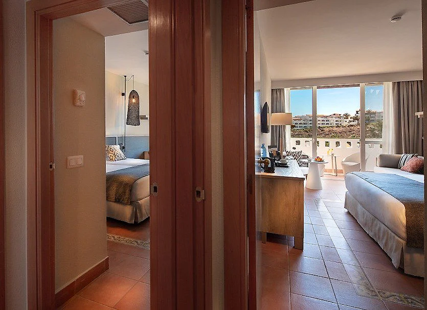 Interior de hotel con sala, sof&aacute;, ventanales y habitaci&oacute;n al fondo