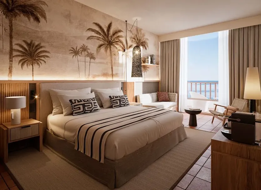 Habitaci&oacute;n de hotel con cama doble y balc&oacute;n, palmeras decorativas al fondo