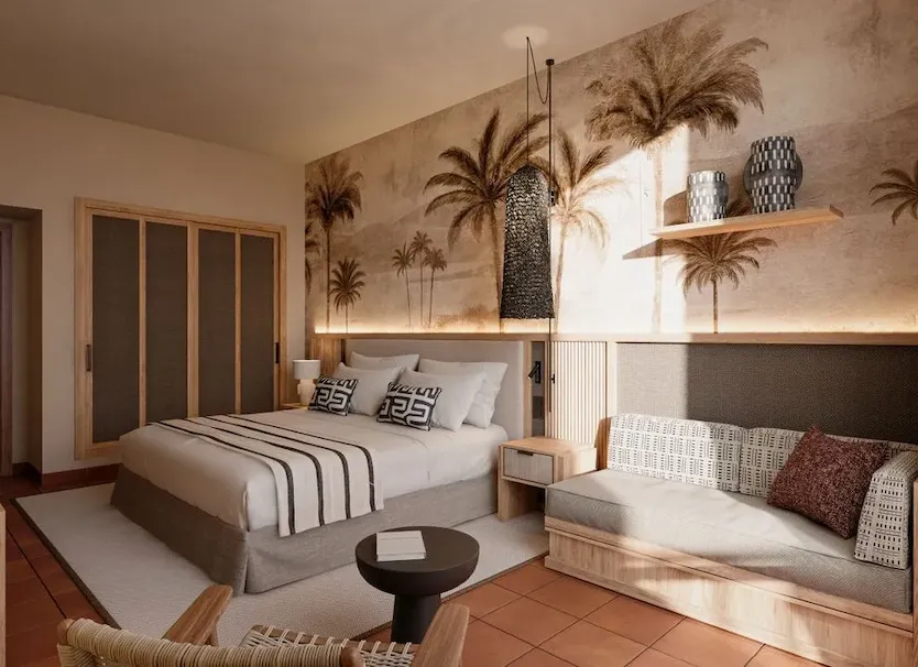 Dormitorio moderno con cama, sof&aacute;, palmeras decorativas y luz natural.