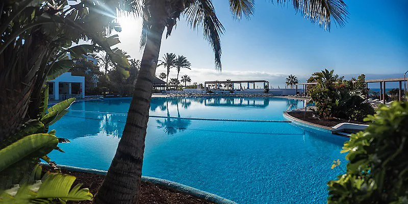 Piscina azul con palmeras y cielo despejado en un resort junto al mar