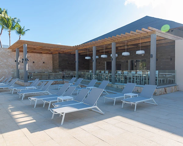 Tumbonas blancas frente a piscina en terraza con p&eacute;rgola y palmeras