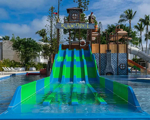 Tobog&aacute;n acu&aacute;tico verde y azul con agua en un parque tropical.