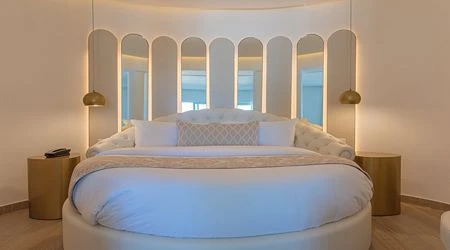 Dormitorio con cama redonda, luz c&aacute;lida y cabecero de arco con columnas.