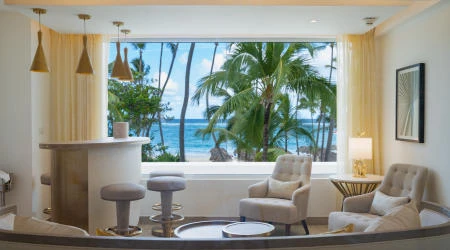 Sala de estar con vista al mar y palmeras, junto a ventana y sillones