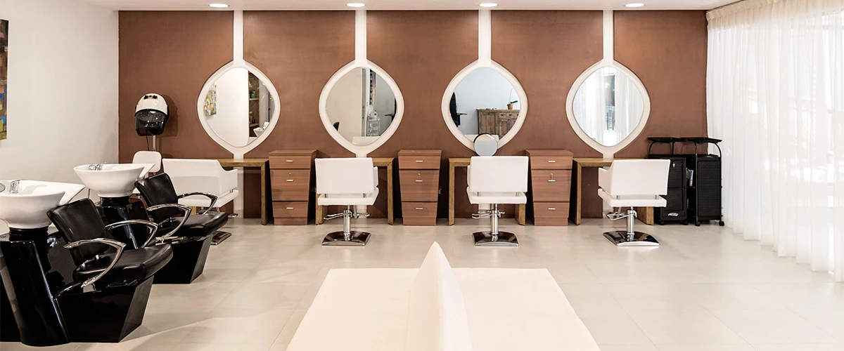 Sal&oacute;n de belleza con sillones negros, mesas blancas y espejos redondos.