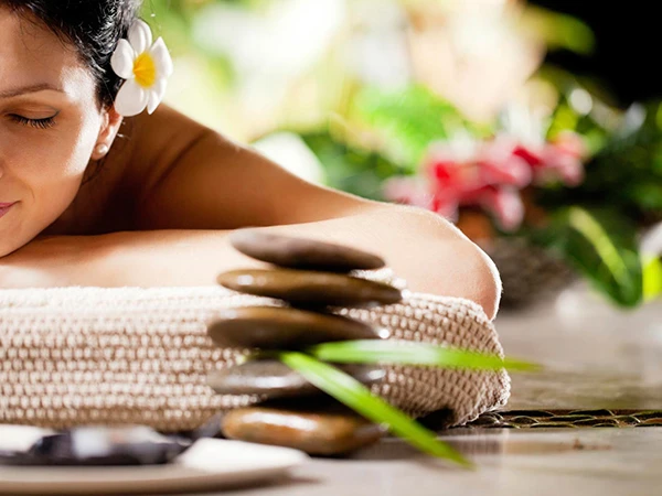 Mujer con flor en el cabello recibe masaje con piedras calientes.