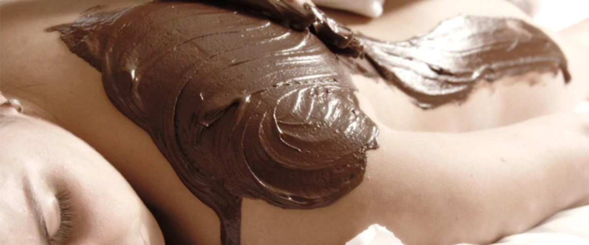 Persona recibiendo masaje con crema de chocolate oscura, en camilla blanca