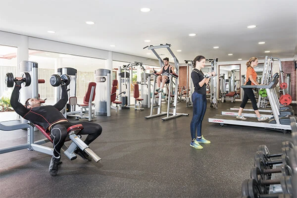 Personas entrenando en un gimnasio con m&aacute;quinas de pesas y poleas.